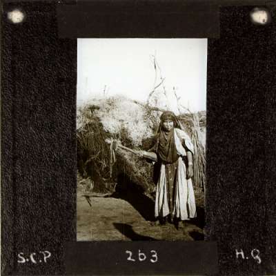 Lantern Slide: Local woman standing by large pile of brushwood
